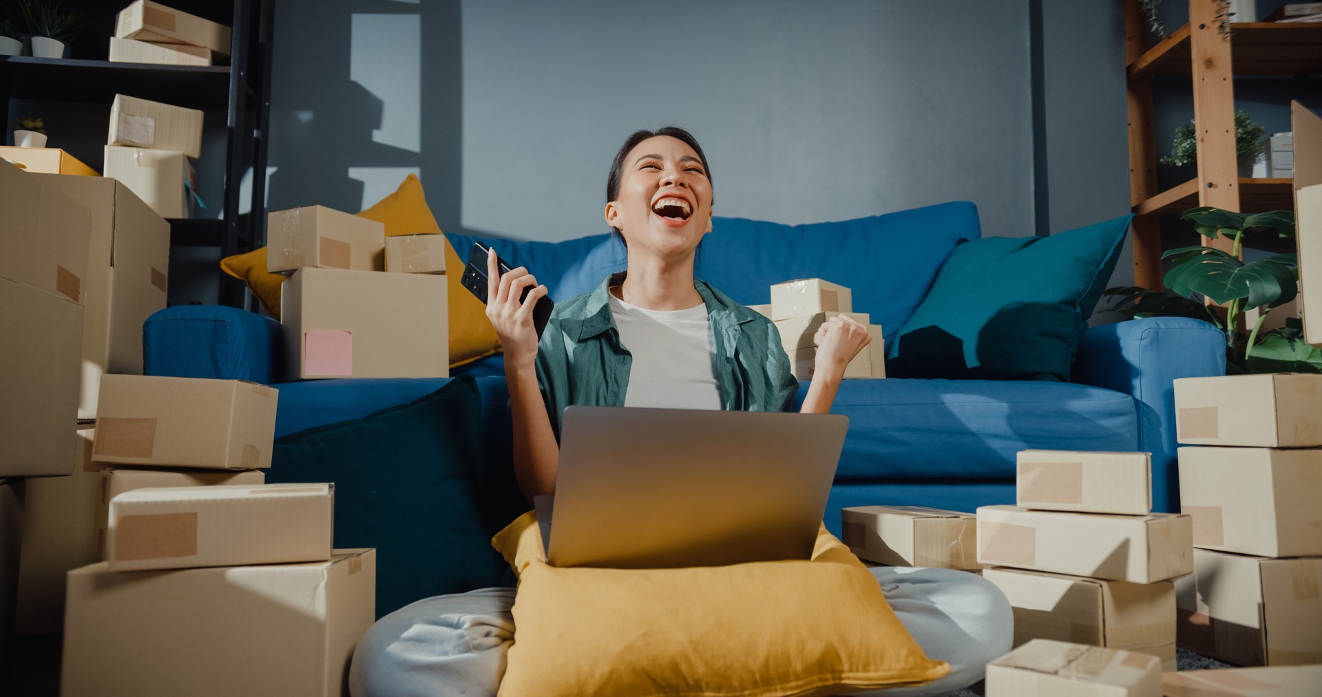 Young Asian female seller worker online store using phone preparing parcel for shipment to client at home.